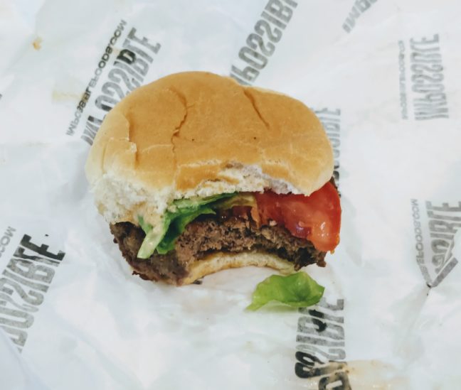 Impossible Burger in a bun with lettuce and tomato on a paper wrapper